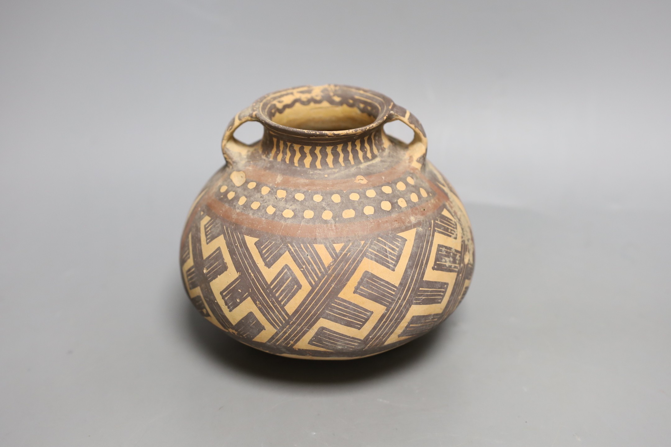 A Chinese pigment painted pottery two handled jar, possibly Neolithic, 14cm high